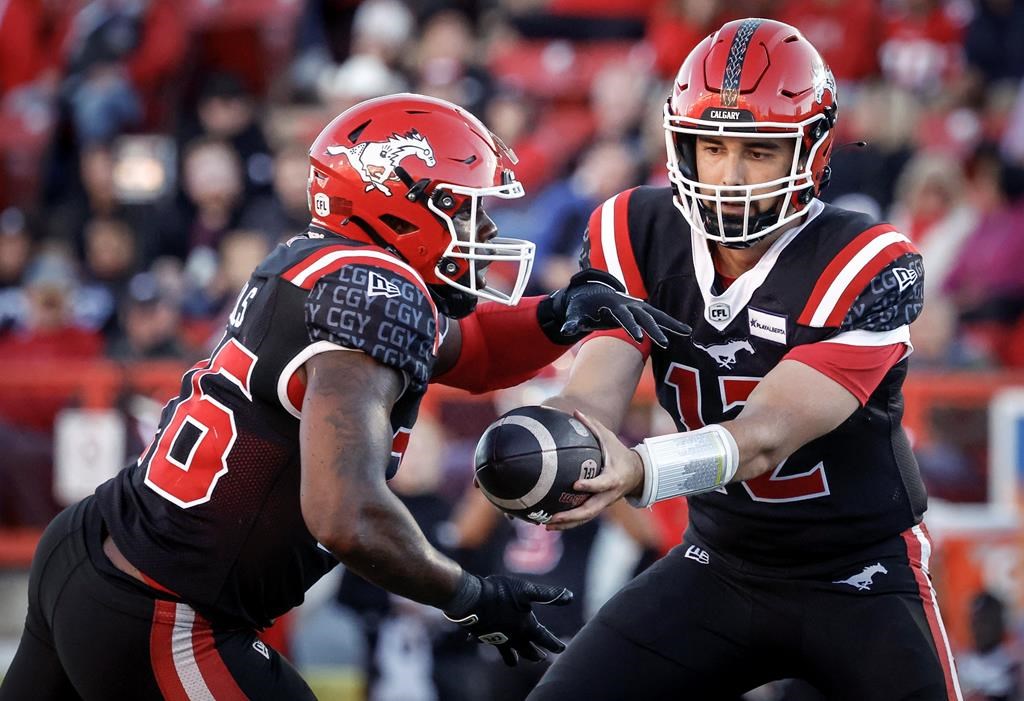 Calgary Stampeders quarterback Jake Maier (12) hands the ball off to Dedrick Mills (26) during second half CFL football action against the Montreal Alouettes in Calgary on September 14, 2024.