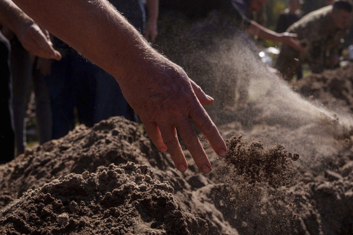 People throw three handfuls of soil into a grave during the funeral ceremony of six Ukrainian servicemen killed in a Russian rocket attack at a Ukrainian military academy, during their funeral ceremony in Poltava, Ukraine, Saturday Sept. 7, 2024. (AP Photo/Evgeniy Maloletka) Evgeniy Maloletka