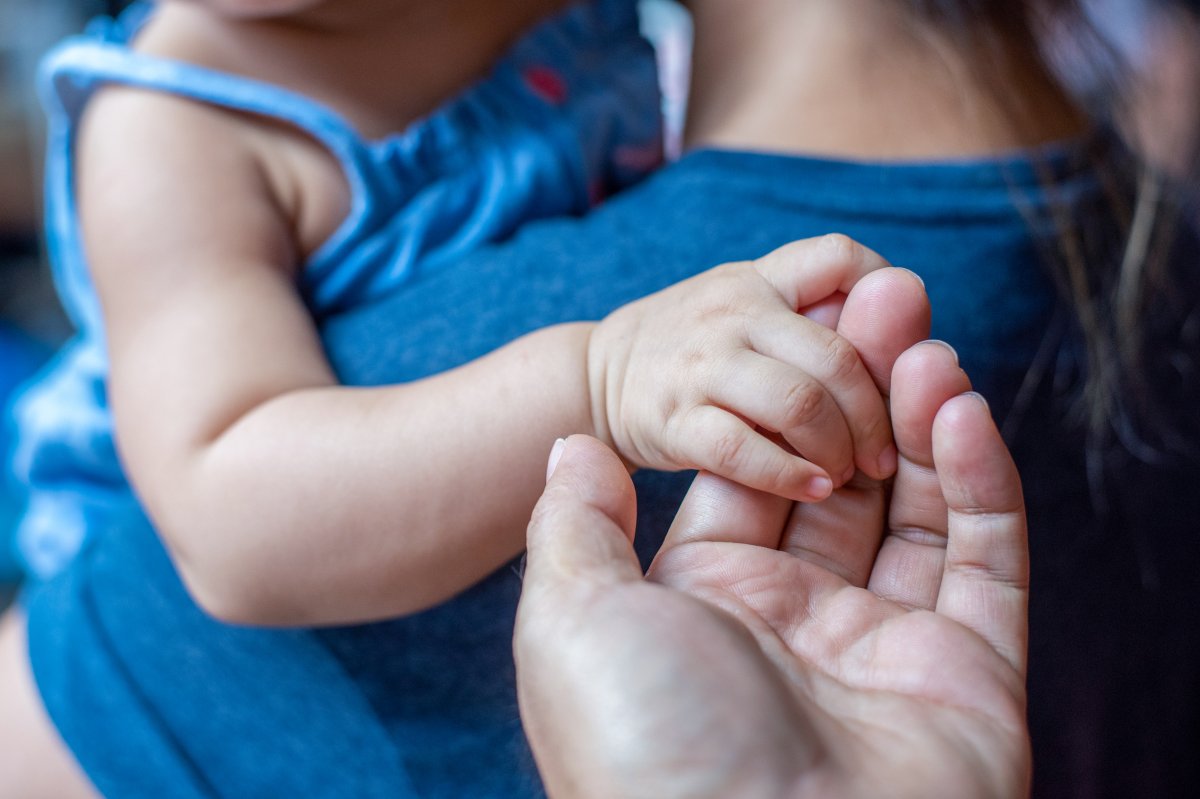 A baby holds an adult's hand.