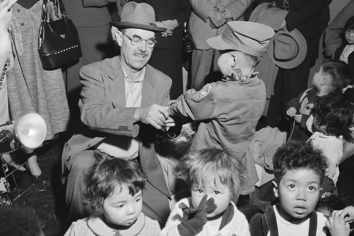 Oregon farmer Harry Holt, left, checks the identification of one of the Korean orphans he brought from South Korea as they arrive in San Francisco, Dec. 17, 1956. (AP Photo/Ernest K. Bennett, File)