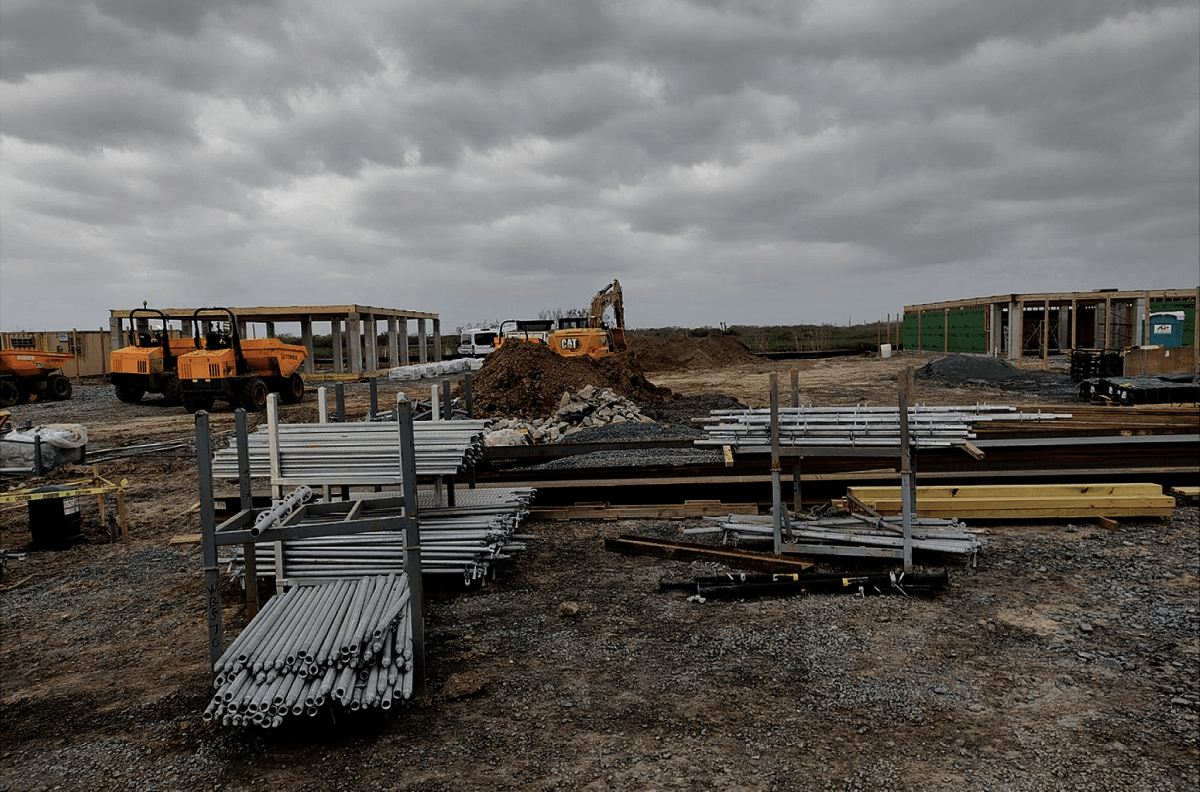 A plot of land crowded with metal beams, scaffolding and construction equipment. There are clouds overhead.