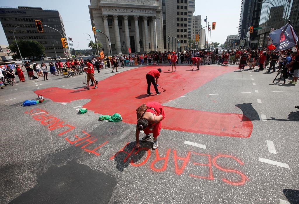 Family and supporters paint a red dress as they gather to protest a lack of action by all levels of governments in funding a search of Winnipeg's landfills for missing Indigenous women, at Portage and Main in Winnipeg, Thursday, Aug. 3, 2023. 