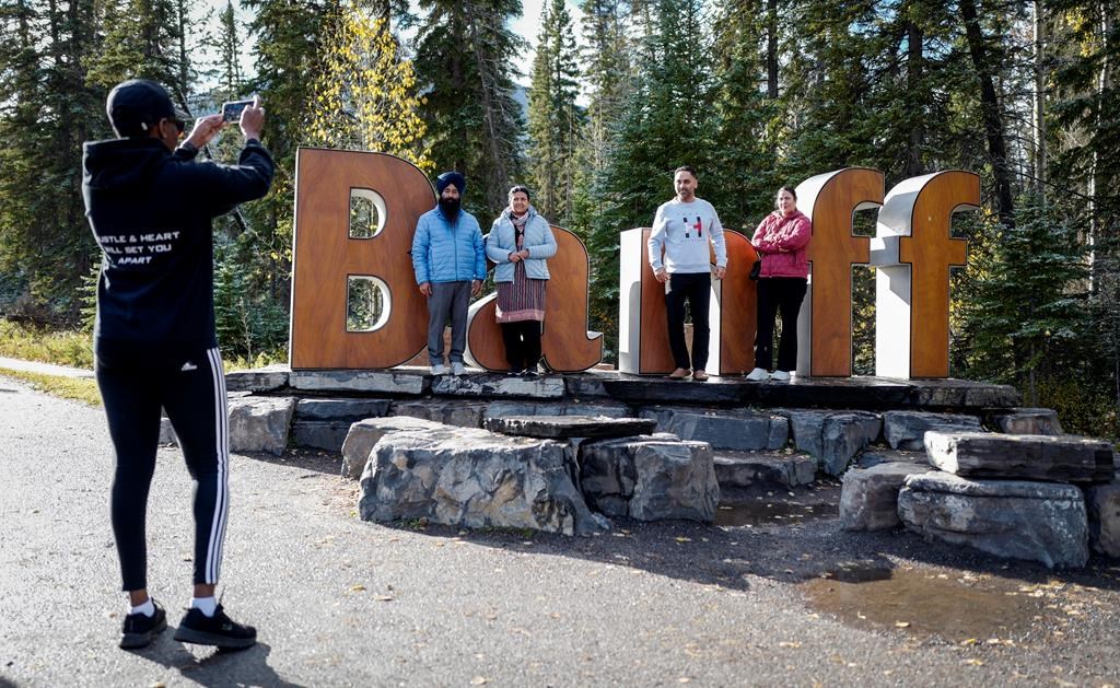 Tourists pose for photos on the iconic Banff sign in Banff, Thursday, Oct. 17, 2024. The town is planning to move the sign in the coming months. 