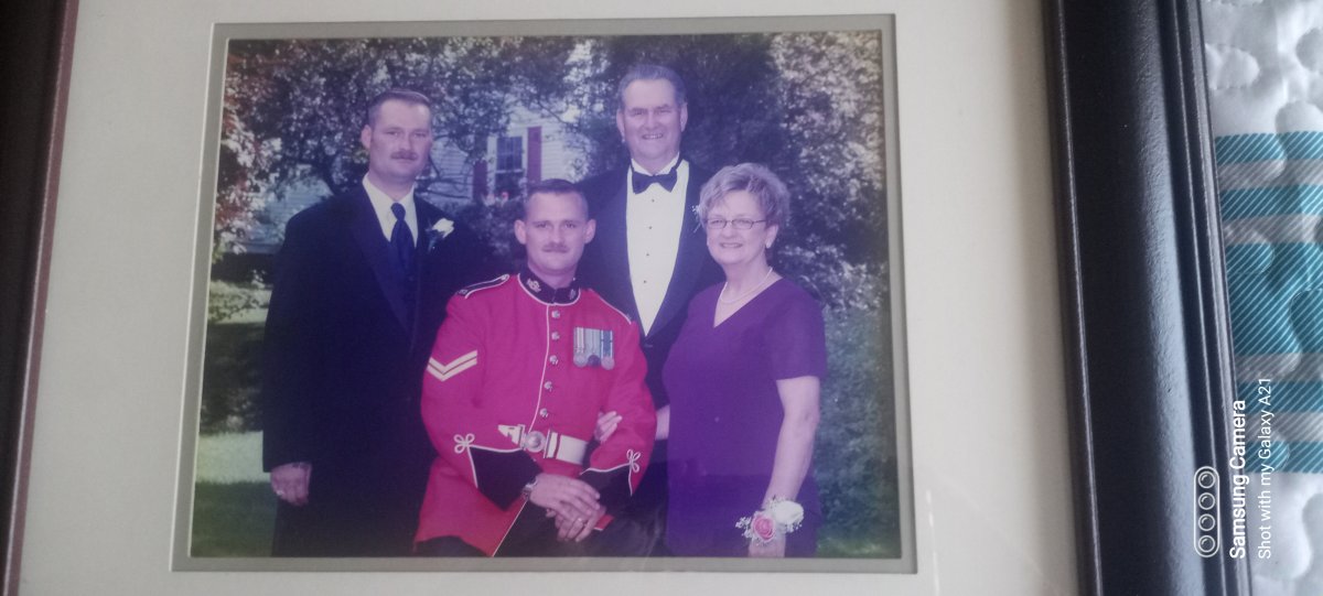 a family poses for a photo dressed for a wedding, one man is dressed in a red military dress uniform