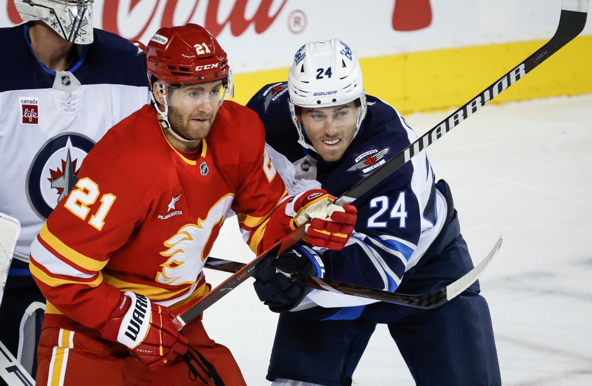 Winnipeg Jets' Haydn Fleury, right, checks Calgary Flames' Kevin Rooney during first period NHL preseason hockey action in Calgary, Alta., Friday, Oct. 4, 2024. THE CANADIAN PRESS/Jeff McIntosh.