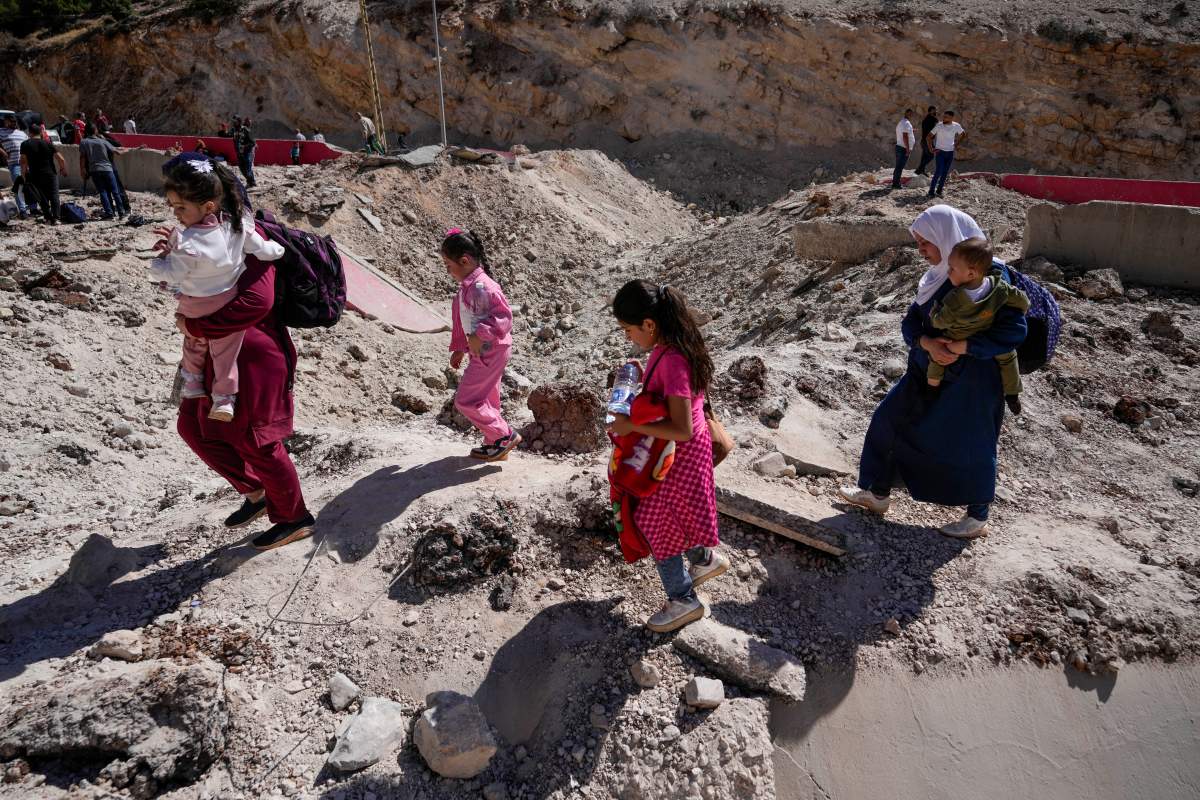 People carry their luggage as they cross into Syria on foot, through a crater caused by Israeli airstrikes aiming to block Beirut-Damascus highway at the Masnaa crossing, in the eastern Bekaa Valley, Lebanon, Saturday, Oct. 5, 2024.