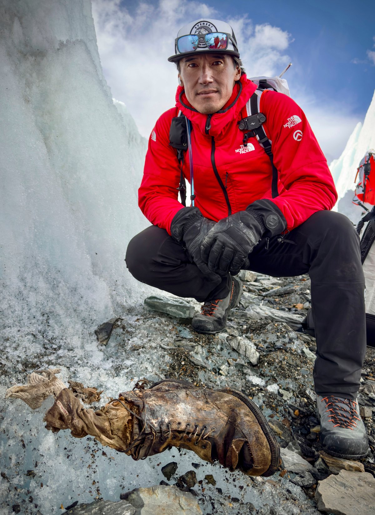 A man in climbing gear stands in front of an old boot in the ice.