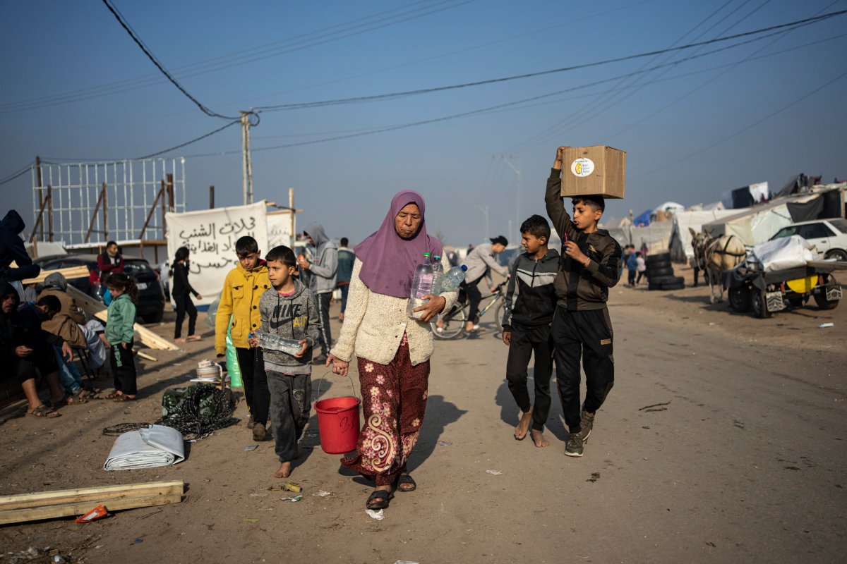 Awatif Abu Jarad, center, who was displaced by the Israeli bombardment of the Gaza Strip, carries filled water bottles with her nephews at a makeshift tent camp in the Muwasi area, southern Gaza, Monday, Jan. 1, 2024. (AP Photo/Fatima Shbair)