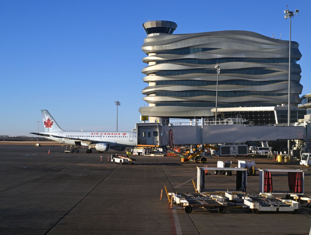 An Air Canada passenger jet is pictured beneath the air traffic control tower and offices at the Edmonton International Airport in Edmonton, Alberta on December 28, 2023.