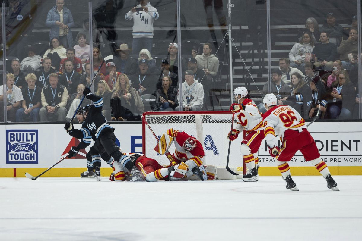 Calgary Flames defenceman Brayden Pachal's (94) skate goes across goaltender Dustin Wolf's (32) face mask and blocks his view against a shot by Utah Hockey Club centre Clayton Keller (9) during the third period of an NHL hockey game, Wednesday, Oct. 30, 2024, in Salt Lake City.