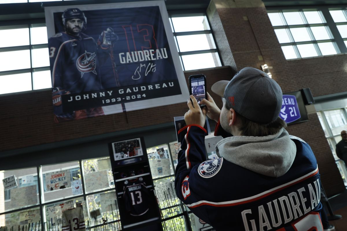 Troy Ward, of Dayton, takes photos of a memorial of Columbus Blue Jackets' Johnny Gaudreau and his brother Matthew before the start of an NHL hockey game against the Florida Panthers. Tuesday, Oct. 15, 2024, in Columbus, Ohio.