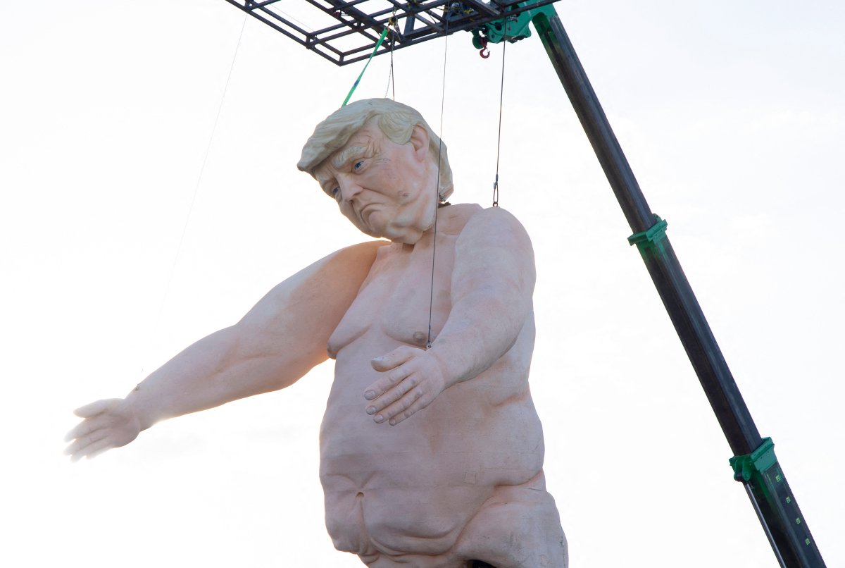 A large statue of Donald Trump, naked, held upright by a crane.