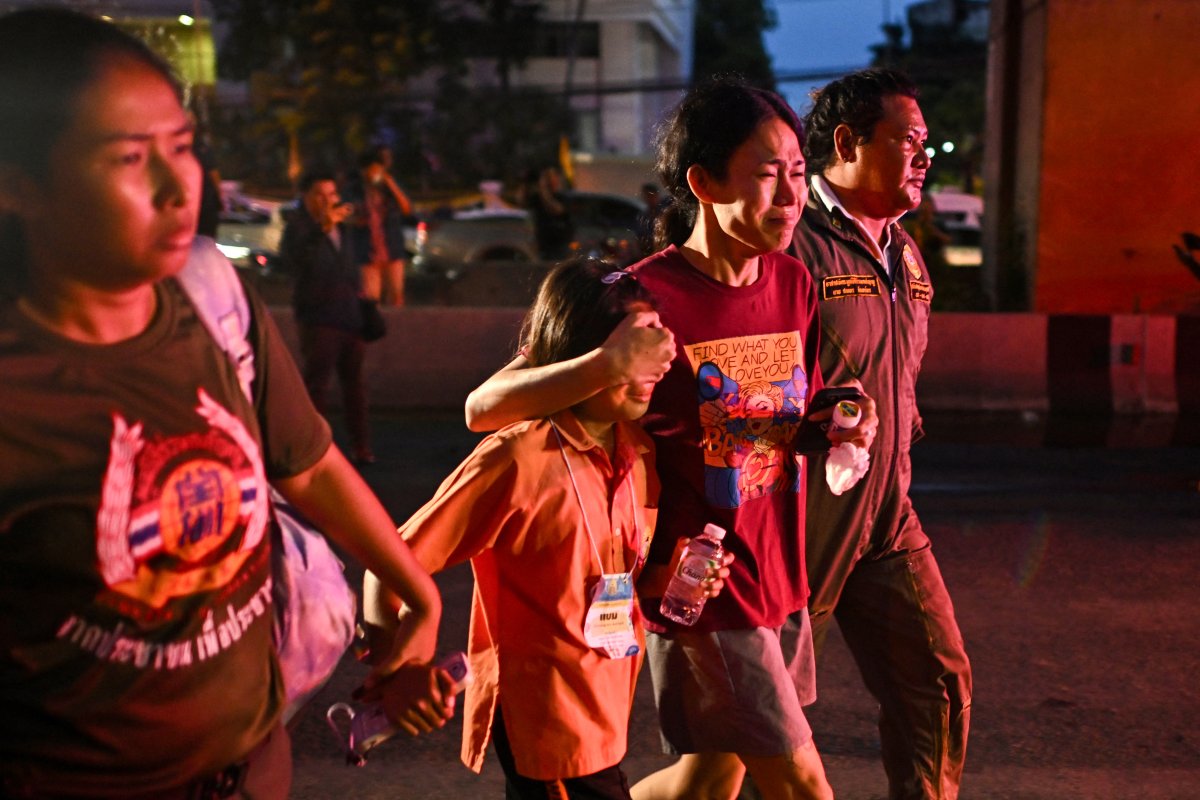 A woman covers the eyes of a young girl as they walk alongside family members in the evening light. They are all crying.