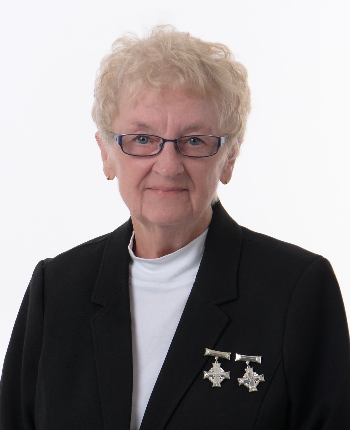 a woman with white hair wears a black blazer with two silver crosses on her right side