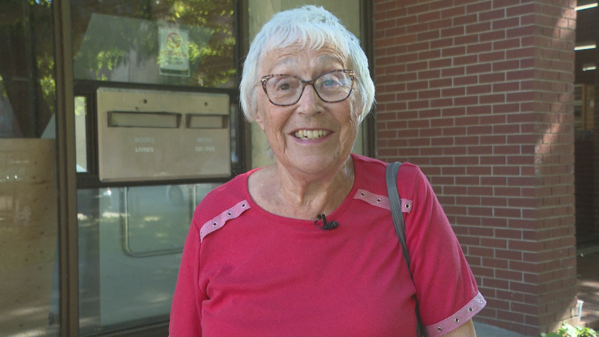 A woman with white hair, glasses and a pink shirt smiles at the camera.