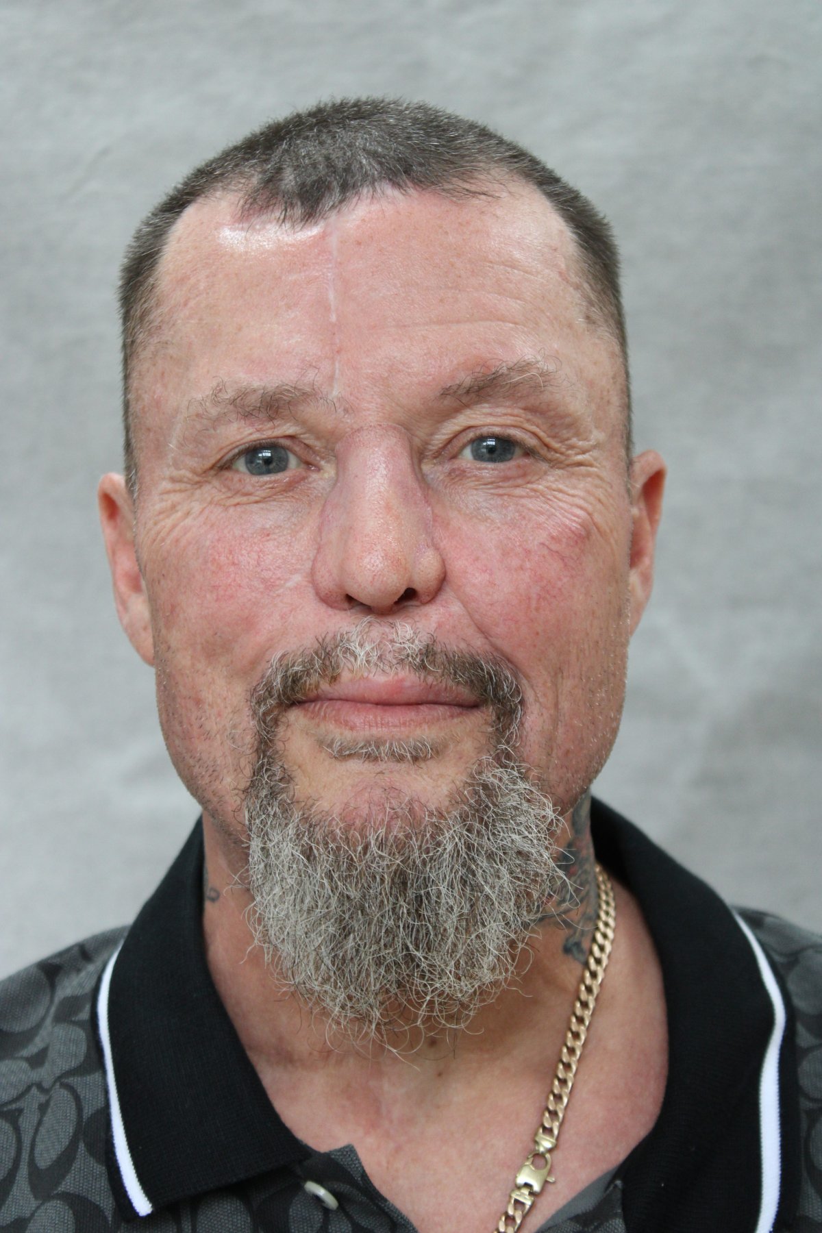 A man with a grey goatee and black collared shirt smiles.