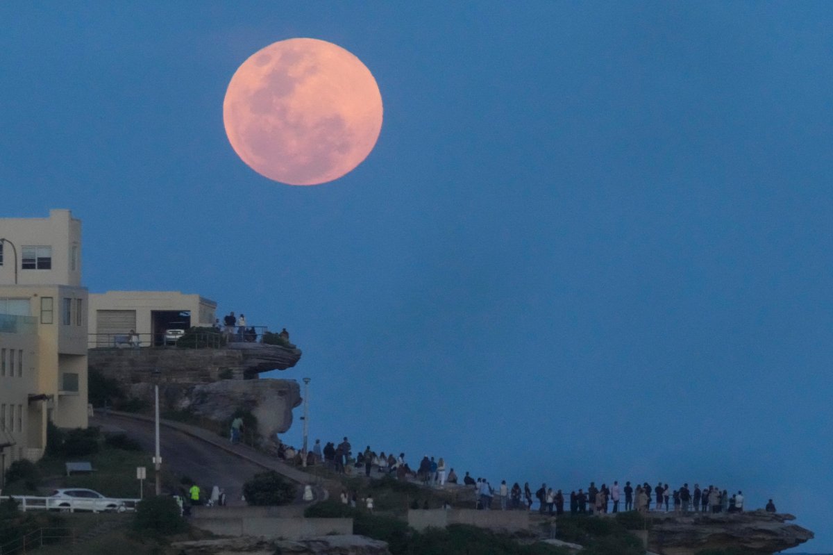 People watch from a cliff top as the moon rises at Bondi Beach in Sydney, Australia, Thursday, Oct. 17, 2024. (AP Photo/Mark Baker)