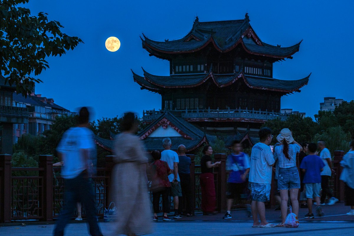 a full moon rises as visitors tour a scenic area during the Mid-Autumn Festival in Huzhou City in east China's Zhejiang Province, Tuesday