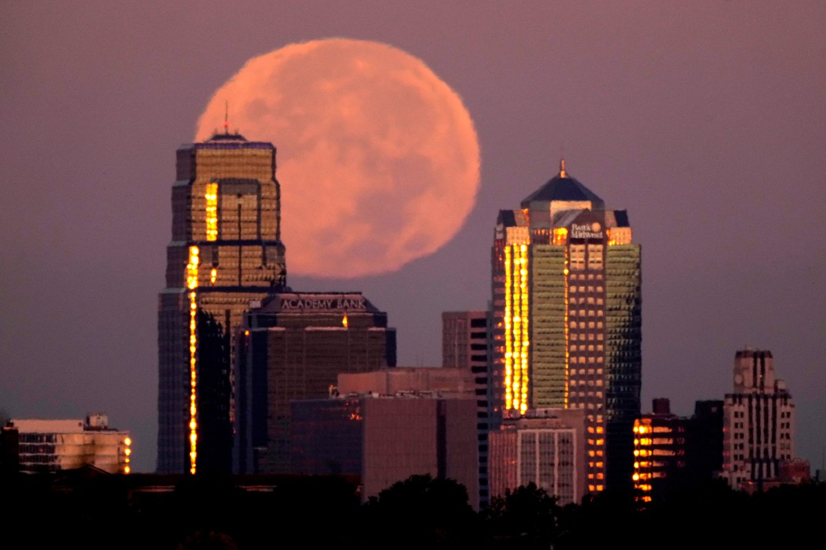 The moon rises beyond downtown buildings Thursday