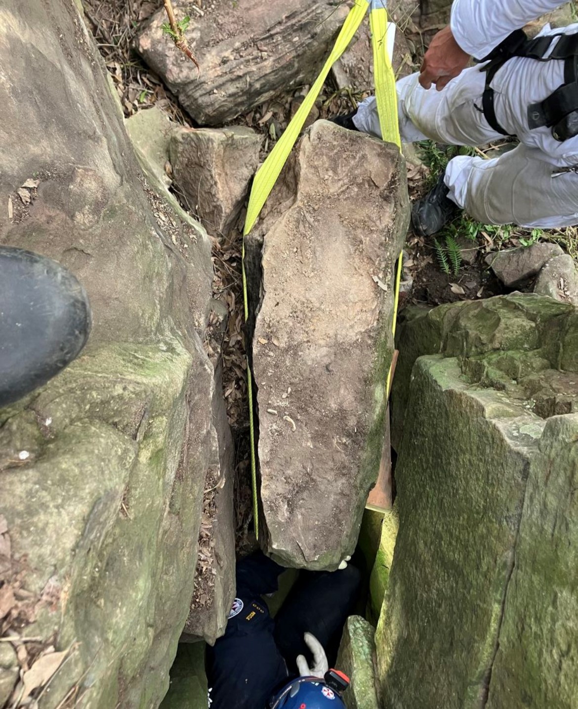 A rock being hoisted between other rocks using a rope and pulley system.