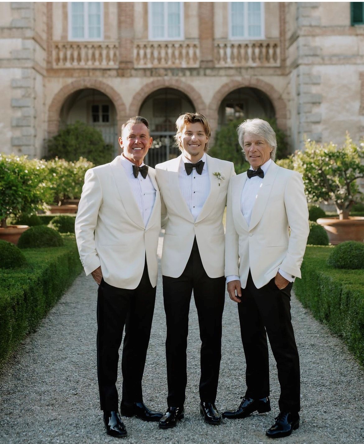 Three men stand in white tuxedos. One is Jake Bongiovi, one is Jon Bon Jovi.