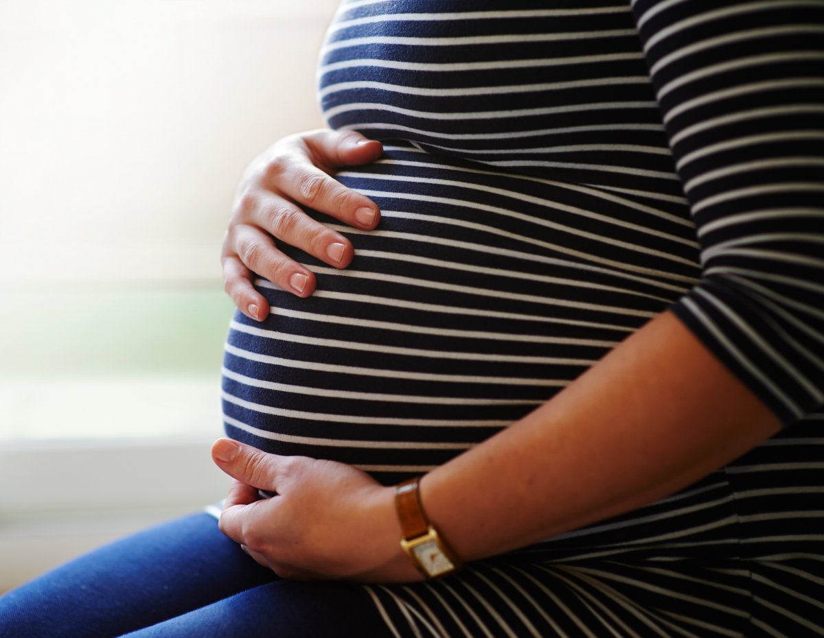 Heavily pregnant female sitting by window, holding her bump with both hands.