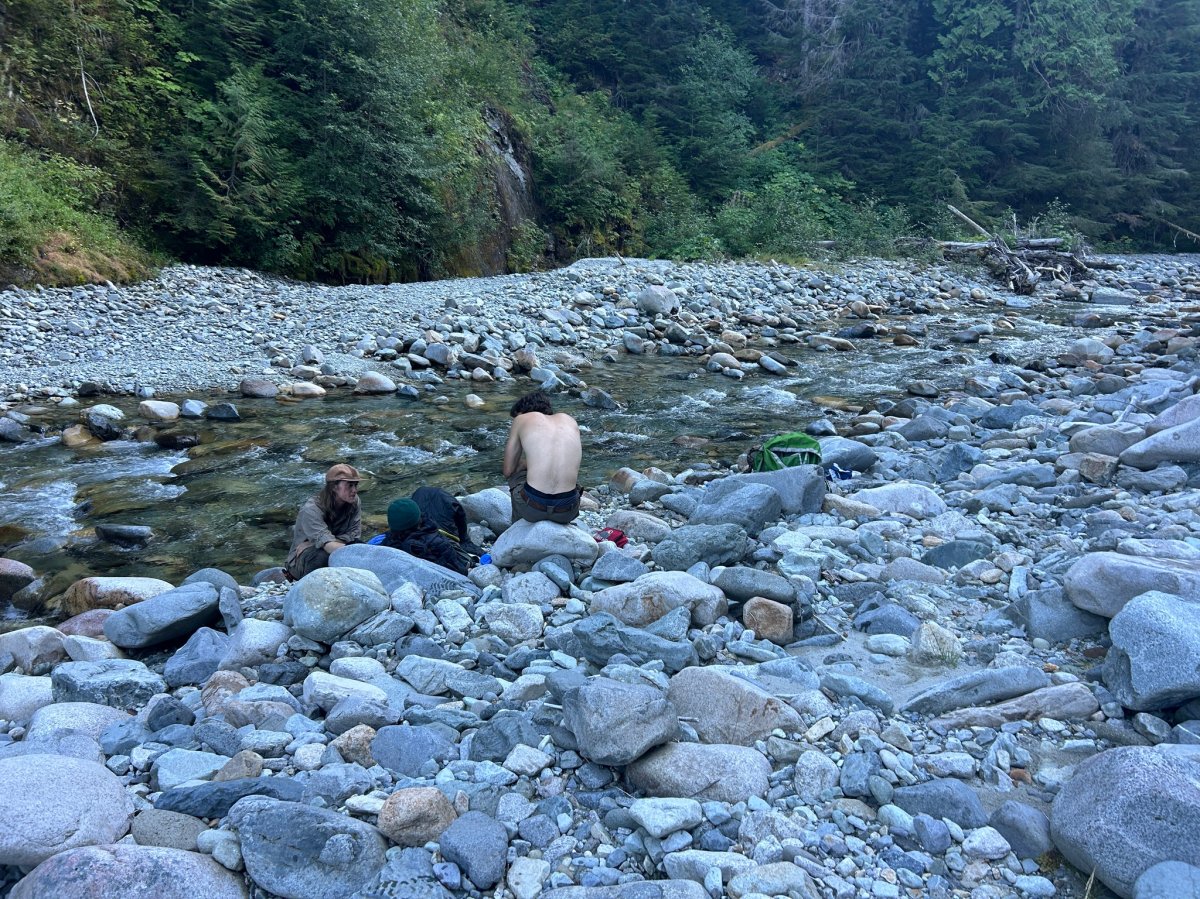 Pacific Northwest Trail Association trail crew members on the bank of the Chilliwack River tend to Robert Schock (not visible).