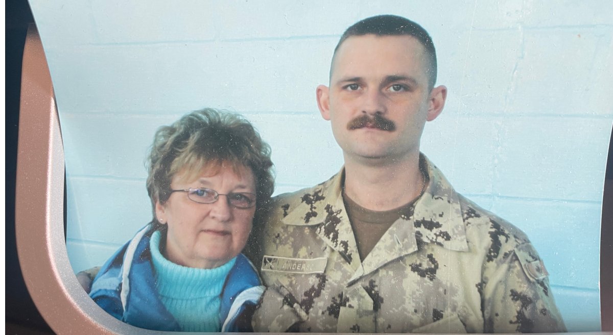 A woman in a blue coat stands next to a young man with a moustache wearing combat fatigues