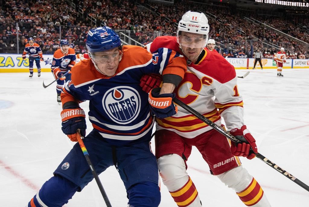 Calgary Flames' Mikael Backlund (11) and Edmonton Oilers' Travis Dermont (24) battle for the puck during first period NHL action in Edmonton, Sunday, Oct. 13, 2024.