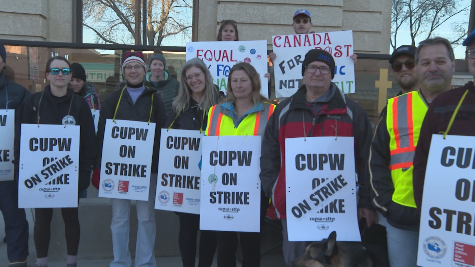 A row of postal workers picketing in a row with signs.