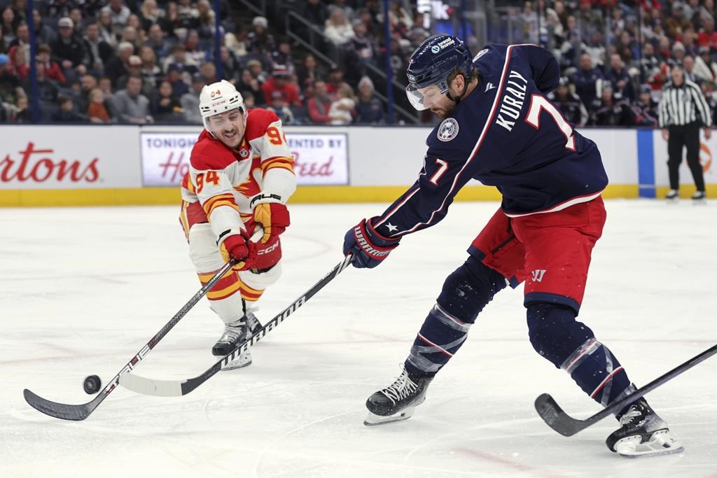 Columbus Blue Jackets forward Sean Kuraly, right, shoots the puck in front of Calgary Flames defenceman Brayden Pachal during an NHL hockey game in Columbus, Ohio, Friday, Nov. 29, 2024.