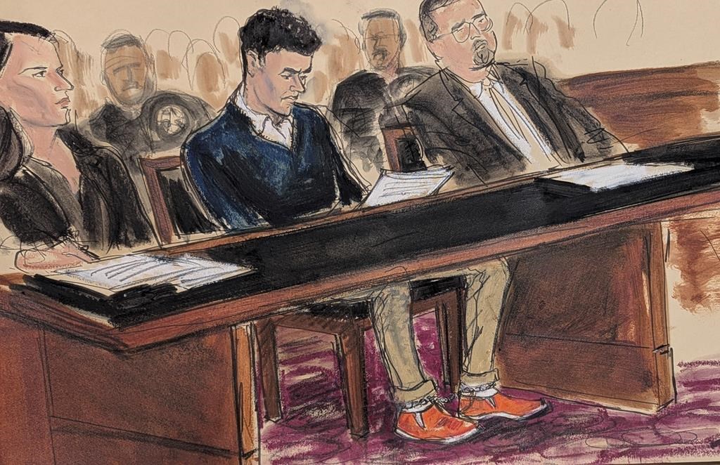 Luigi Mangione, center, sits in court reading the federal complaint while wearing orange slip on shoes and his ankles shackled in Manhattan federal court, Thursday, Dec. 19, 2024, in New York. He is flanked by his attorneys, Karen Agnifilo, left, and Marc Agnifilo.