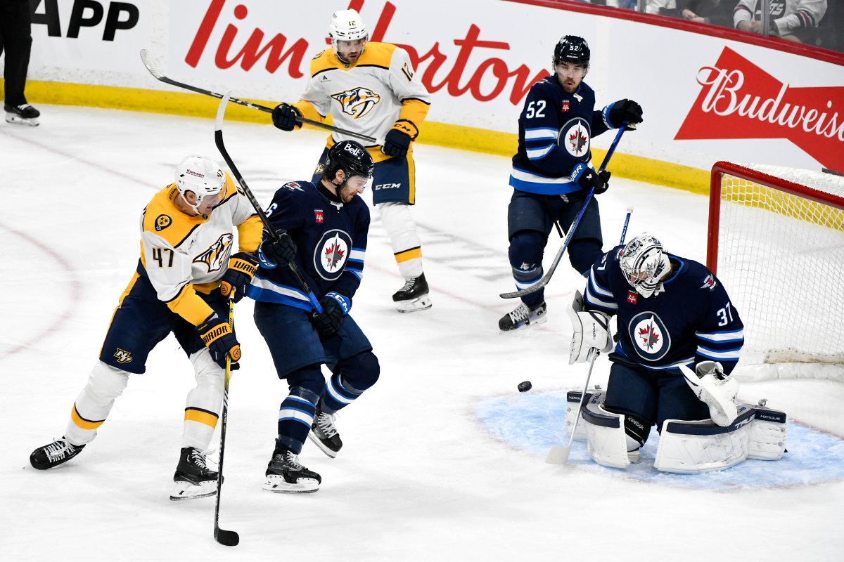 Winnipeg Jets goaltender Connor Hellebuyck (37) makes a save on a shot by Nashville Predators' Michael McCarron (47) as he is defended by Colin Miller (6) during the first period of their NHL hockey game in Winnipeg, Monday, Dec. 30, 2024. THE CANADIAN PRESS/Fred Greenslade.