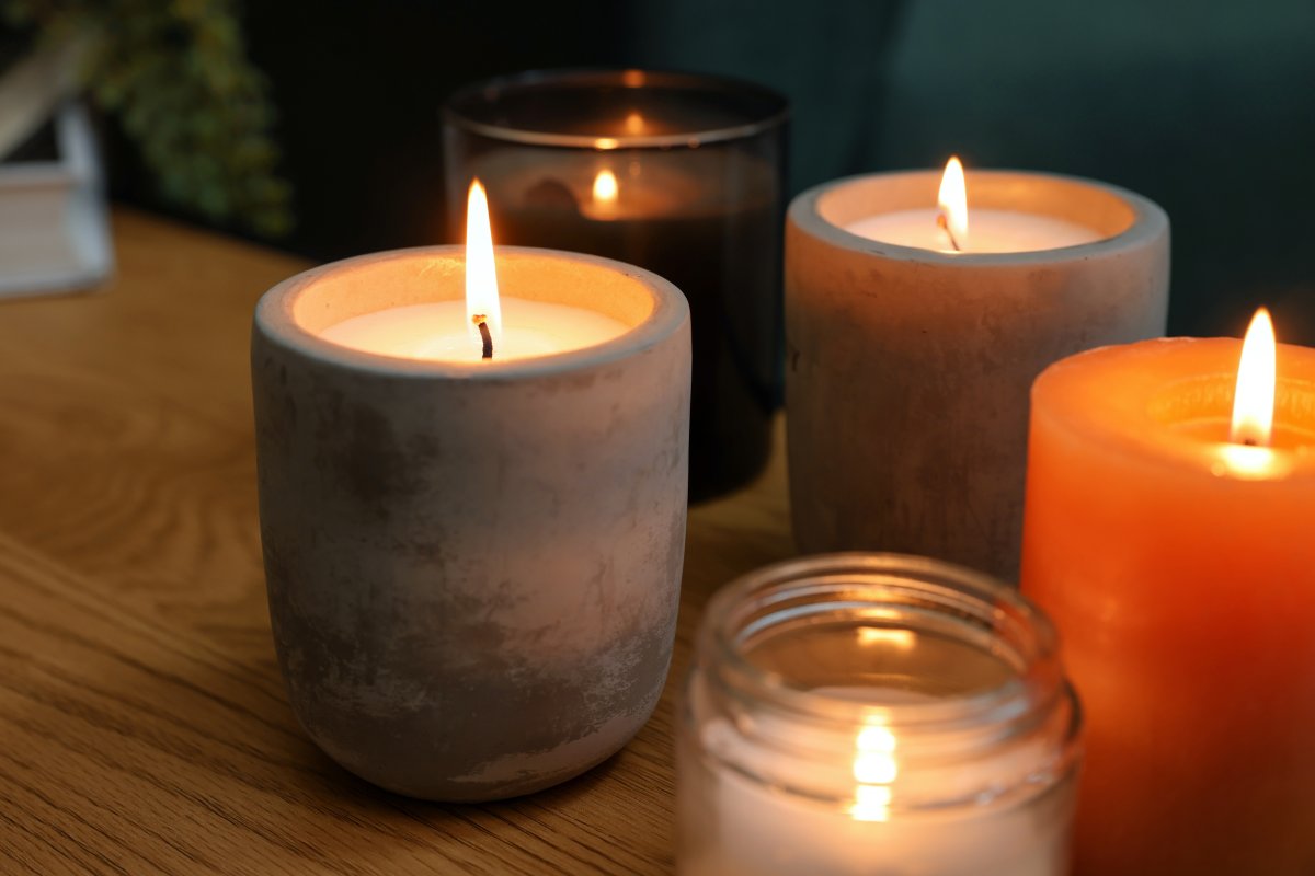 Lit candles in different holders on wooden table indoors