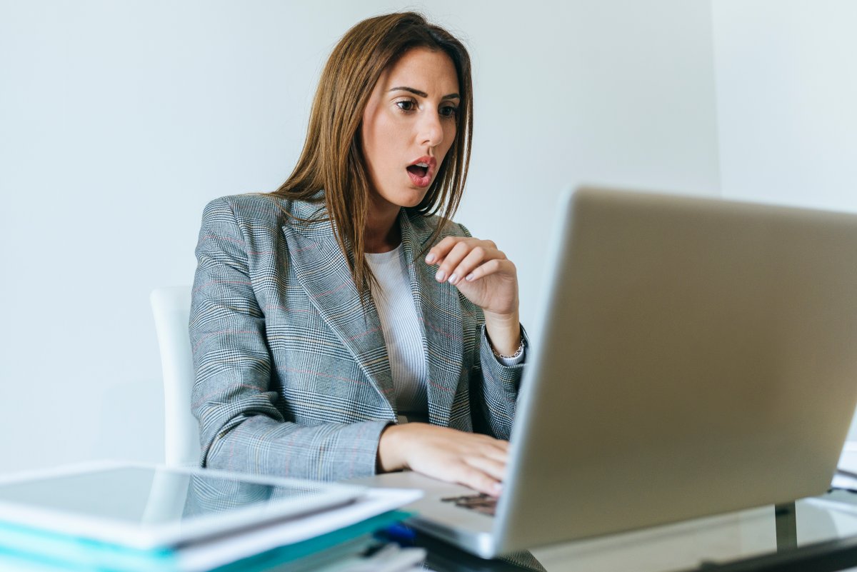 A woman with a surprised look on her face as she reads a message on her laptop.