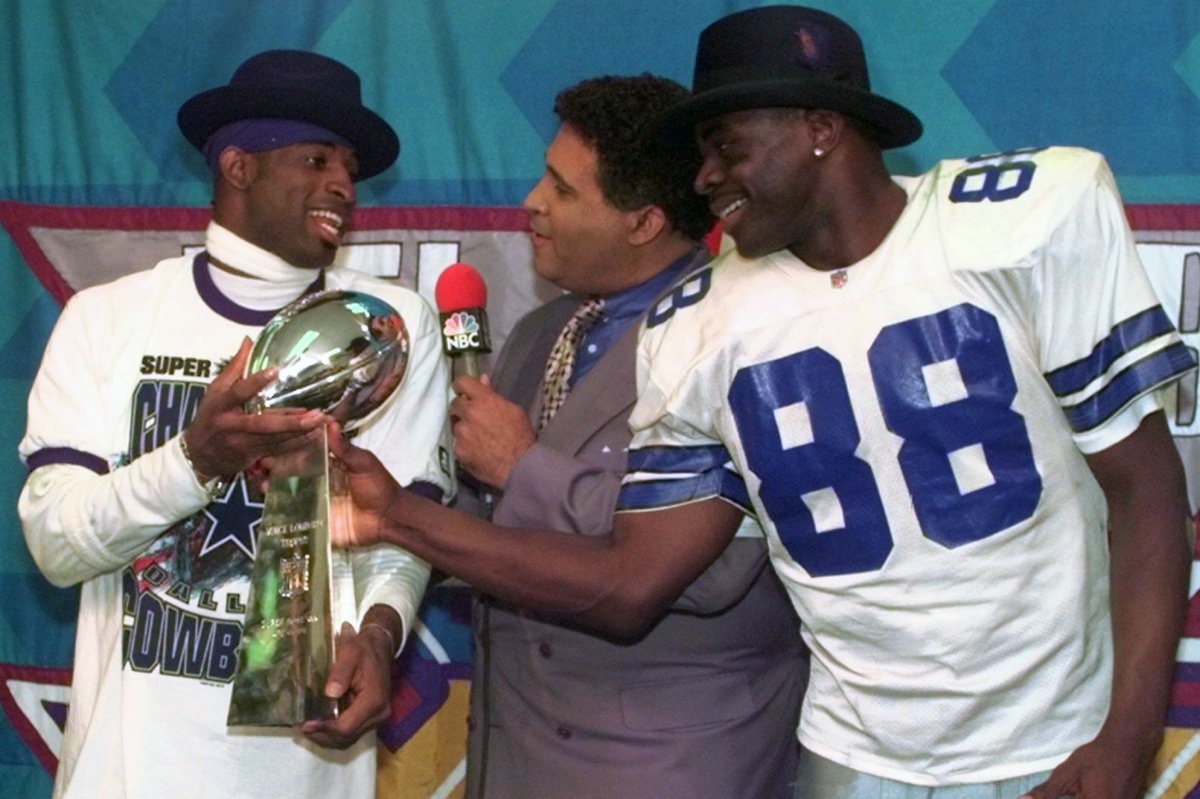 FILE - Dallas Cowboys cornerback Deion Sanders, left, and running back Michael Irvin (88) share the Vince Lombardi trophy as NBC commentator Greg Gumbel interviews the two after Super Bowl XXX in Tempe, Ariz., Sunday, Jan. 28, 1996.