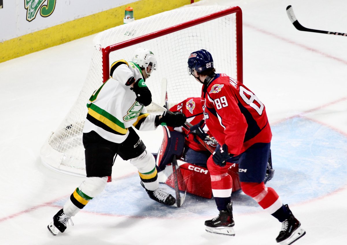 Landon Sim of the London Knights pushes a puck through the legs of Windsor Spitfires goaltender Joey Costanzo in a game between London and Windsor at Canada Life Place on Dec. 13, 2024.