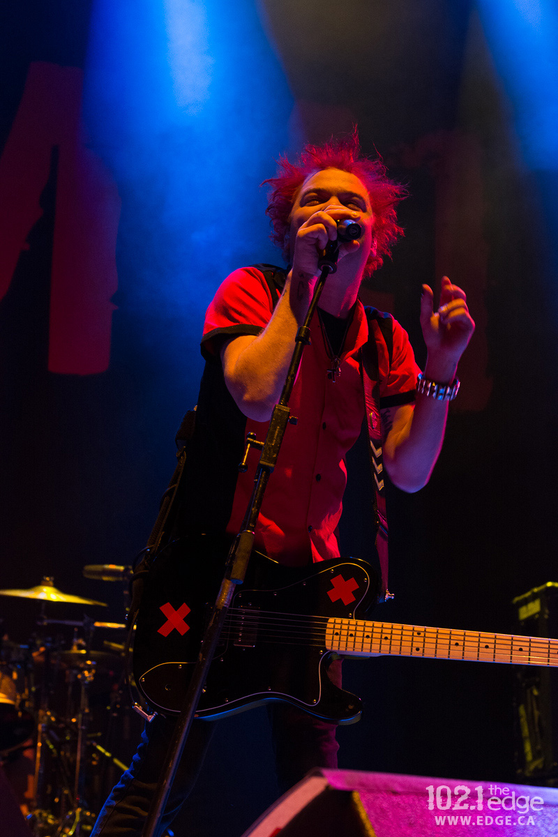 Deryck Whibley stands on stage singing into a microphone.