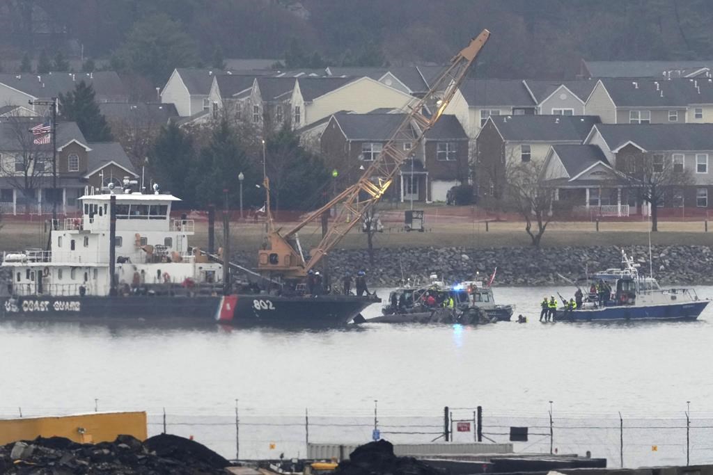 A member of a dive team and a Coast Guard vessel with a crane are pictured as they work near the wreckage of a Black Hawk helicopter in the Potomac River from Ronald Reagan Washington National Airport, Friday, Jan. 31, 2025, in Arlington, Va.