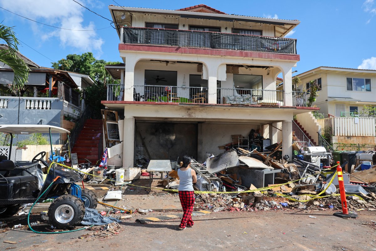 A woman stands in front of the home where a New Year's Eve fireworks explosion killed and injured people, Wednesday, Jan. 1, 2025, in Honolulu. (AP Photo/Marco Garcia).