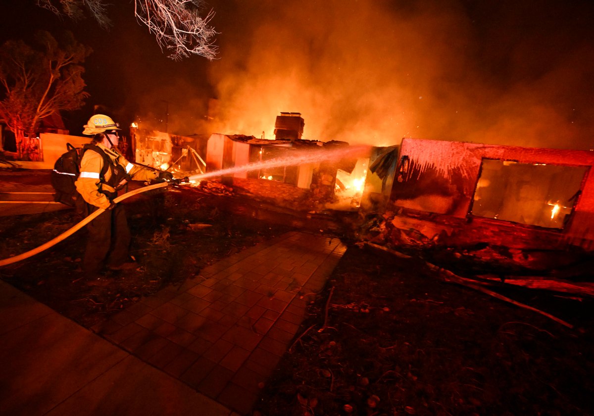 A firefighter from Costa Mesa works to extinguish a fire burning a home on Valleylights Drive during the Eaton fire in the Hastings Ranch community of Pasadena, California.