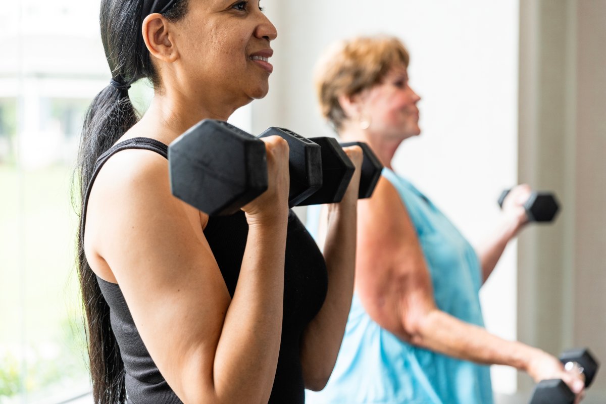 The mid adult female uses dumbbells to strength train with her mom at the gym.