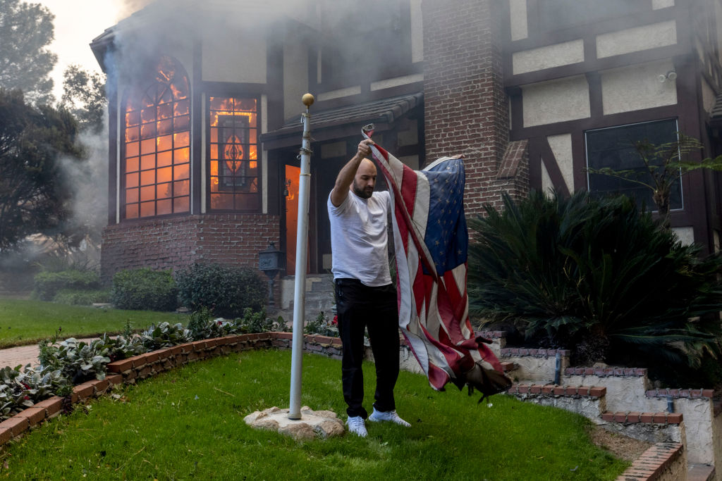 A resident takes down an American flag outside a burning house during the Eaton Fire in Altadena, Calif., on Jan. 8, 2025.