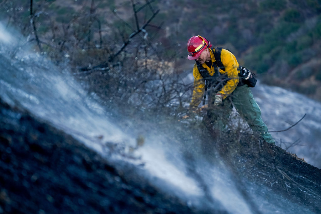 A firefighter works on a hillside during the aftermath of the Palisades Fire in the Pacific Palisades area of Los Angeles, Calif., on Sunday, Jan. 12, 2025. At least two rounds of vicious, dry Santa Ana winds are expected to blast through Southern California early this week, bringing powerful gusts that will challenge fire crews struggling to contain two destructive blazes and likely force thousands more residents to evacuate.