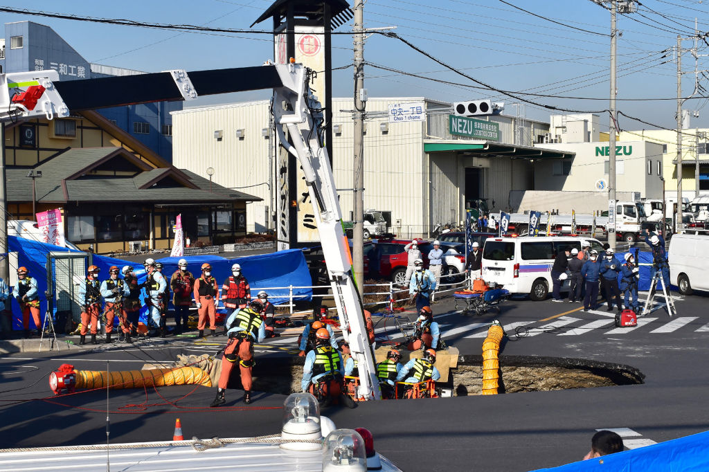 Firefighters work to rescue a truck driver after his vehicle was swallowed up by a sinkhole at a prefectural road intersection, in the city of Yashio, Saitama Prefecture on January 28, 2025.