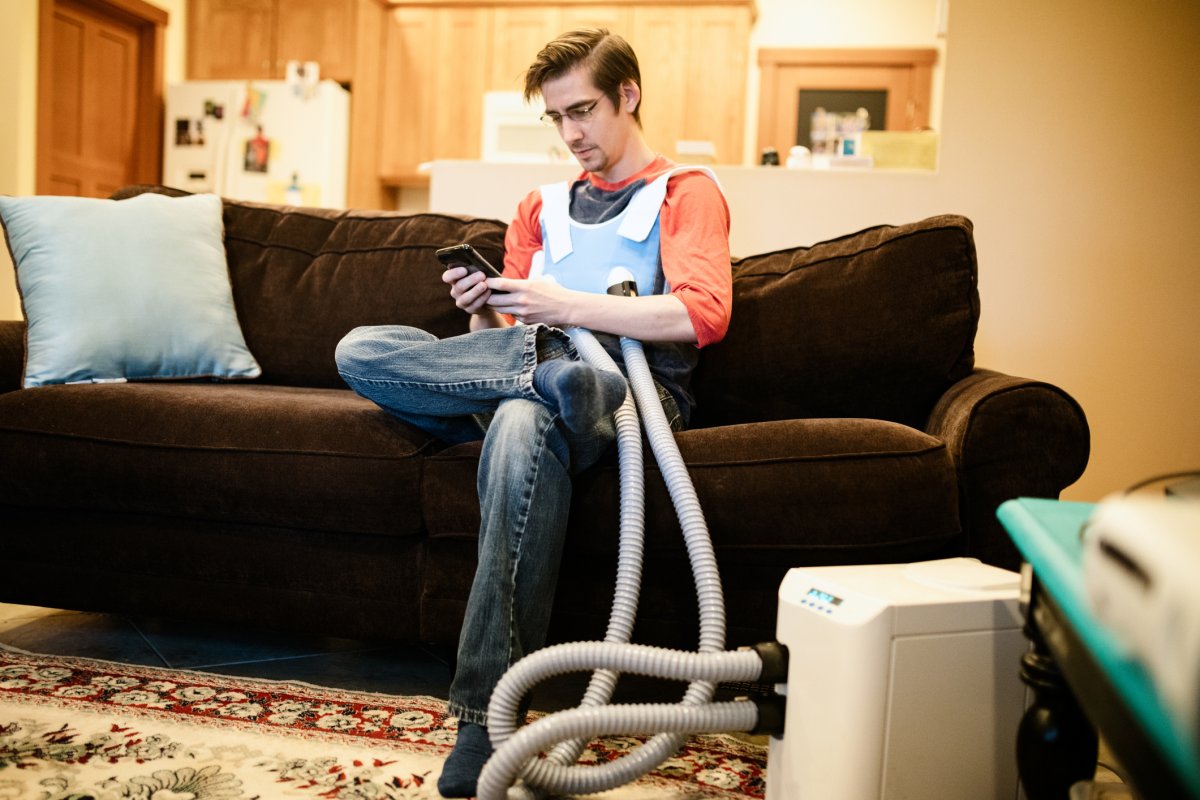 A man looks at his phone while using a machine that assists with mucus buildup caused by cystic fibrosis.