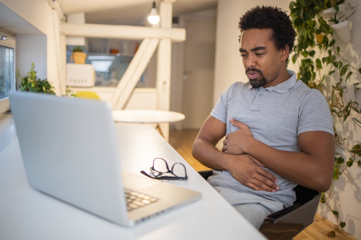 A man clutches his stomach while staring at a laptop