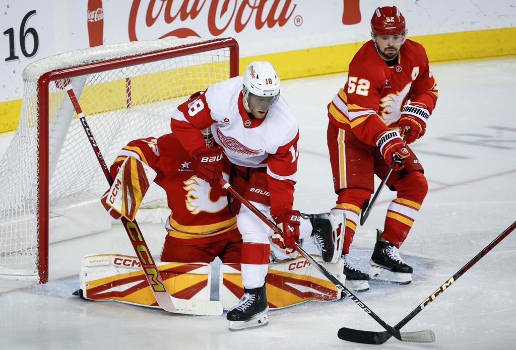 Detroit Red Wings’ Andrew Copp, centre, crashes into Calgary Flames goalie Dustin Wolf, hidden, as MacKenzie Weegar checks during second period NHL hockey action in Calgary, Alta., Saturday, Feb. 1, 2025. THE CANADIAN PRESS/Jeff McIntosh
