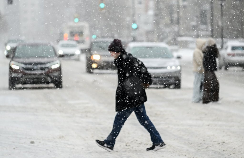 A person crosses a street as snow falls in Montreal, Sunday, January 7, 2024. THE CANADIAN PRESS/Graham Hughes.