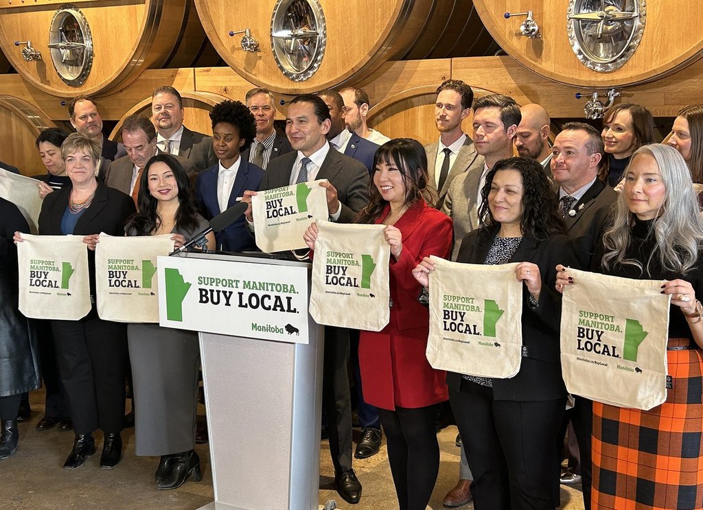 Manitoba Premier Wab Kinew and caucus members hold up tote bags during a press conference encouraging consumers to buy Manitoba goods and services, in Winnipeg, Wednesday, Feb. 5, 2025. THE CANADIAN PRESS/Steve Lambert.